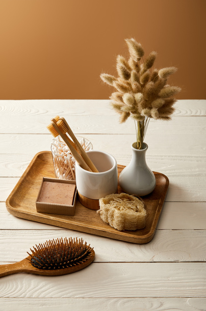 hair brush, wooden tray with vase of spikelets and various hygiene and care items on white wooden surface, zero waste concept - Fotó, kép