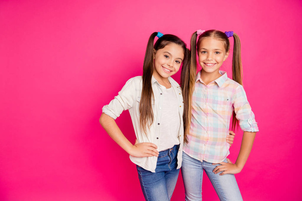 Close up photo two small little age girls best friends buddies hugging toothy smiling sweet wearing casual jeans denim checkered plaid shirts isolated rose vivid vibrant bright background - Фото, зображення