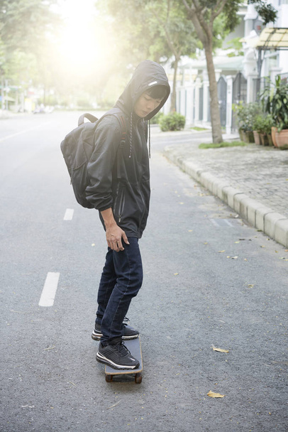 Jeune homme asiatique en vêtements sombres équitation en skateboard
 - Photo, image