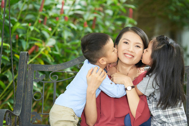 Petits enfants embrassant heureuse jolie mère sur les deux joues
 - Photo, image