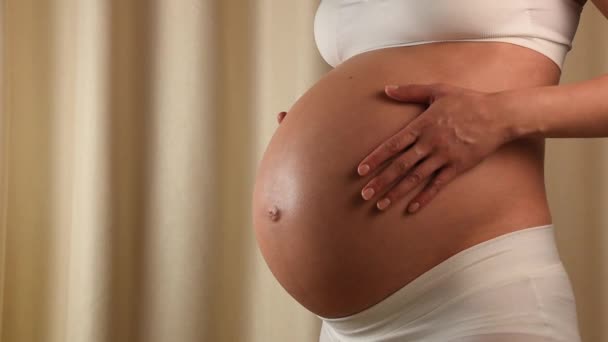 Közelkép a hossz-szelvény nézet terhes kaukázusi nő tartja, és megérintette kitett hasára a kezét a felkészülés a baba születése - Felvétel, videó