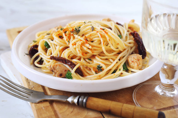 Ιταλική κουζίνα. Σπαγγέτι με λιαστή ντομάτα, σκόρδο ψητό κοτόπουλο και ποτήρι λευκό κρασί. Επιλεκτική εστίαση - Φωτογραφία, εικόνα