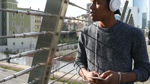 Jonge knappe Amerikaanse Afrikaanse man luisteren muziek met koptelefoon en smartphone in de stad terug lichtstad - Video