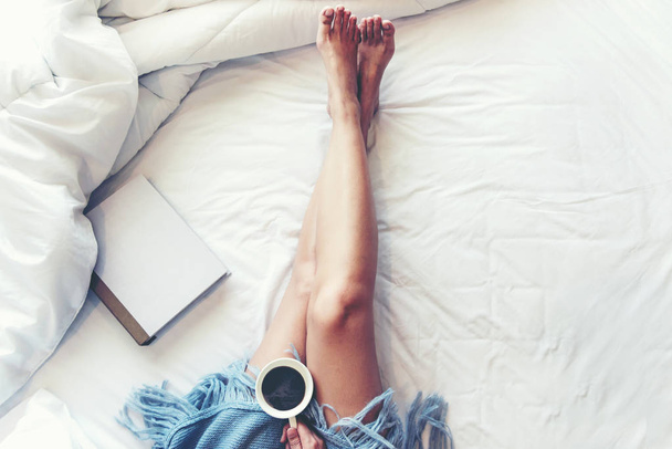 Close up legs women on white bed.  Women reading book and  drinking  coffee in morning relax mood in winter season.   Lifestyle Concept. - Foto, immagini