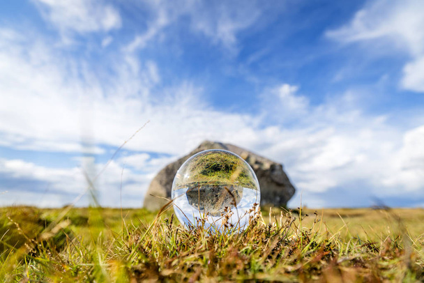 Glass orb op gras met de weerspiegeling van een groot rotsblok in de zomer - Foto, afbeelding