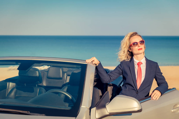 Successful young businesswoman on the beach. Woman standing near the cabriolet classic car. Summer vacations and freedom travel concept - Фото, изображение