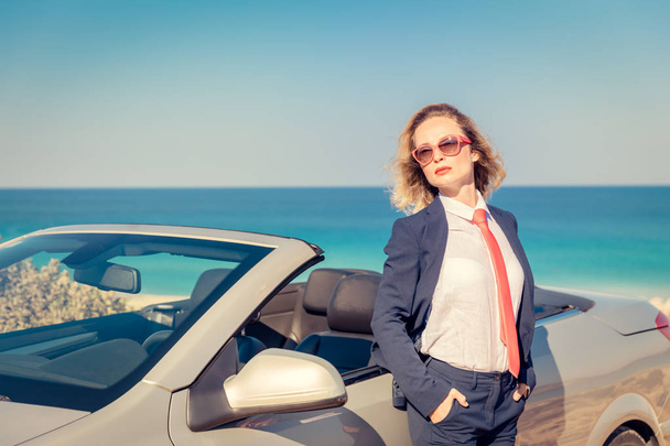 Successful young businesswoman on the beach. Woman standing near the cabriolet classic car. Summer vacations and freedom travel concept - Photo, Image