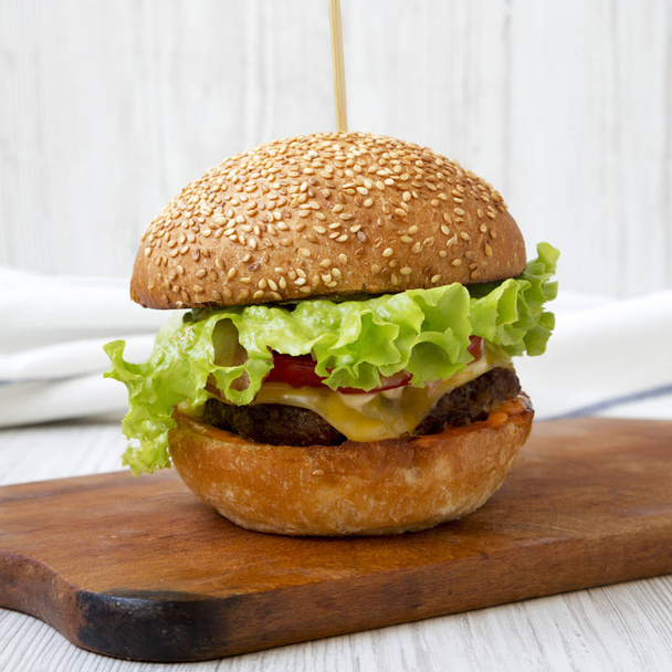 Homemade cheeseburger on rustic wooden board over white wooden background, side view. Closeup. - Fotografie, Obrázek