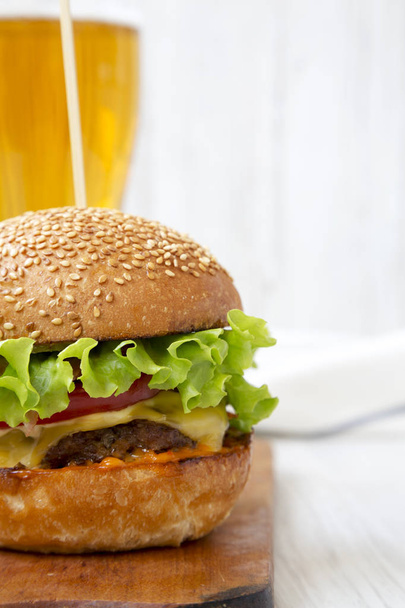 Házi sajtburger és pohár sör rusztikus táblán, fehér fa háttér, oldalnézet. Közeli kép:.  - Fotó, kép