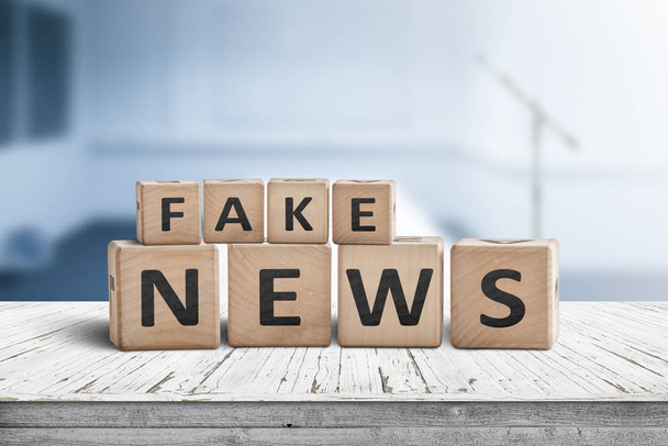 Fake news sign on a wooden desk in a blue room with a blurry background - Photo, Image