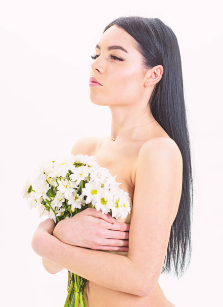 Lady covers breasts with flowers, isolated on white. Woman with smooth healthy skin looks attractive. Girl on calm face stands naked and holds chamomile flowers in front of chest. Skin health concept. - Φωτογραφία, εικόνα
