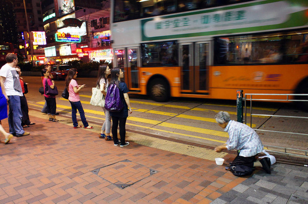 Pedestrians wait for green light to walk across the road next to an elderly woman begging for money in Hong Kong, China, 2 July 2012 - Foto, Bild