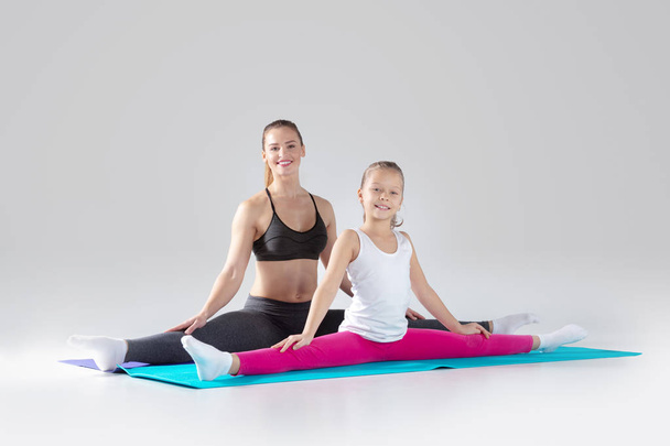Mooie vrouw en haar dochtertje zijn het doen van oefeningen op matten - Foto, afbeelding