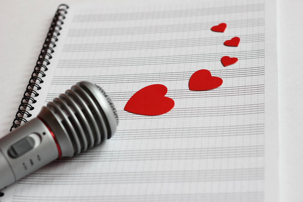 Microphone and paper red hearts are located on a clean music notebook. The concept of music and love. Valentines day - Photo, image