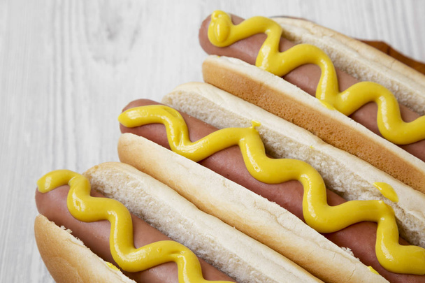 Hot-dog with yellow mustard on wooden board on white wooden background, low angle view. Close-up. - Photo, Image