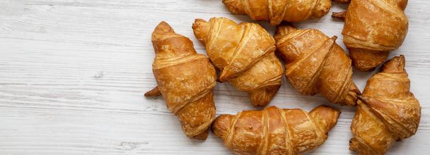 Freshly baked golden croissants on white wooden surface, top view. Flat lay, from above, overhead. Copy space. - Foto, afbeelding