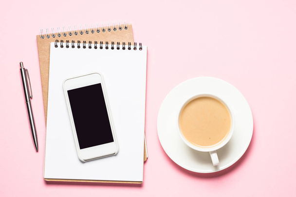 Homeoffice-Arbeitsplatz mit Notizblock, Smartphone und Kaffeetasse auf rosa Schreibtisch. - Foto, Bild