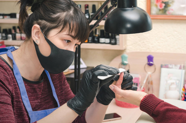 Manucure en gants de latex noir formant la forme d'un ongle de client dans un salon de beauté
. - Photo, image