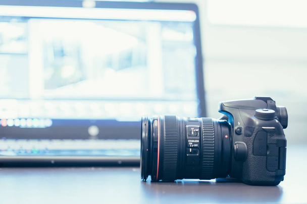 Professional camera with telephoto lens on a table, laptop in the blurry background - Fotoğraf, Görsel