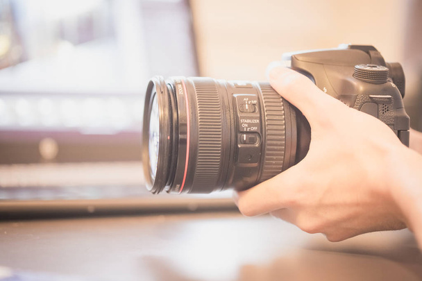 Professional camera with telephoto lens on a table, laptop in the blurry background - Foto, Imagem