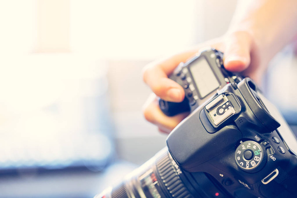 Photographe tient un appareil photo professionnel avec téléobjectif dans sa main, ordinateur portable dans le fond flou
 - Photo, image