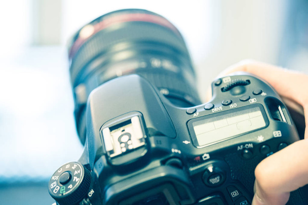 Photographer is holding a professional camera with telephoto lens in his hand, laptop in the blurry background - Photo, image