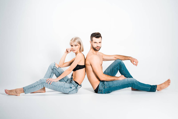 beautiful girlfriend and handsome boyfriend in underwear and jeans sitting back to back on grey - Zdjęcie, obraz