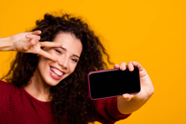Close-up portrait of her she nice attractive cheerful wavy-haired lady holding in hands cell taking making selfie showing v-sign near eye black screen isolated on bright vivid shine orange background - Fotografie, Obrázek