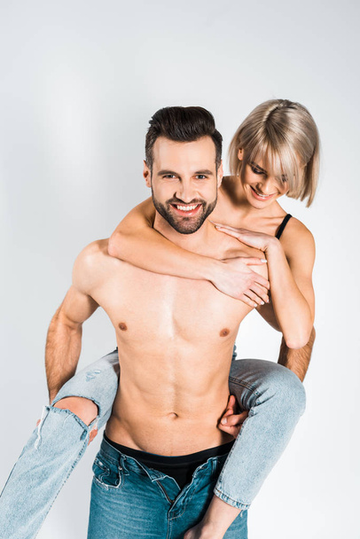 smiling shirtless boyfriend piggybacking beautiful happy girlfriend isolated on grey - Fotografie, Obrázek