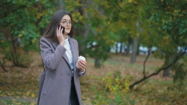 smiling woman drinking coffee and talking over mobile phone in autumn park - Footage, Video