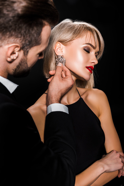 man touching elegant earrings of attractive woman isolated on black - Foto, Imagem