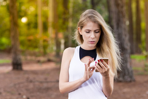 Bella bionda giovane donna nel parco al tramonto controllare i messaggi sul suo cellulare - Immagine
 - Foto, immagini
