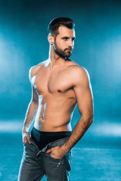 sexy muscular man in black underwear and jeans posing on blue smoky background - Fotó, kép