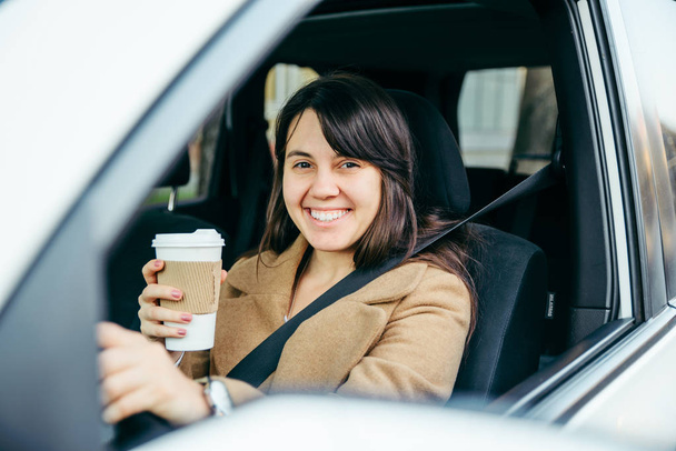 jeune femme souriante conduisant une voiture. ceinture de sécurité. boire du café
 - Photo, image