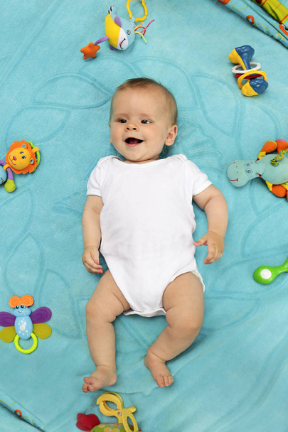 Un pequeño bebé recién nacido está acostado en una manta azul y jugando con juguetes en un estado de ánimo muy divertido
. - Foto, Imagen