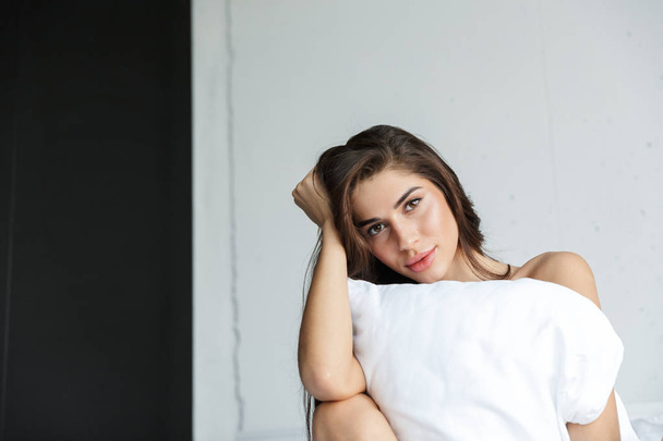 Foto de una hermosa morena increíble vistiendo lencería en casa en el interior sentada en la cama sosteniendo almohada
. - Foto, Imagen