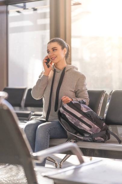 Νεαρή όμορφη γυναίκα που μιλάει με κινητό τηλέφωνο σε μοντέρνα φως αεροδρόμιο. - Φωτογραφία, εικόνα
