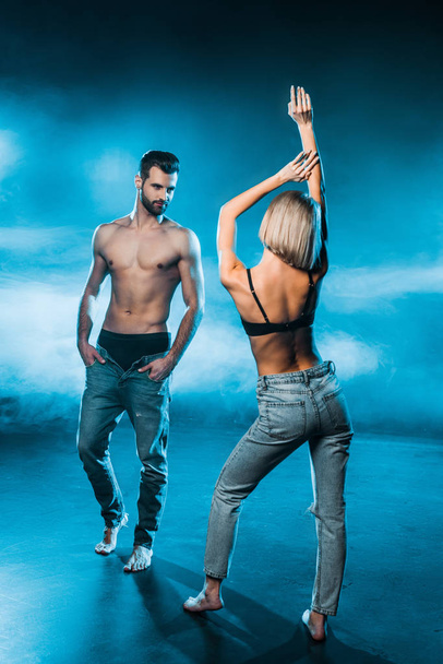 sensual couple in jeans and underwear posing on blue smoky background - Foto, Imagem