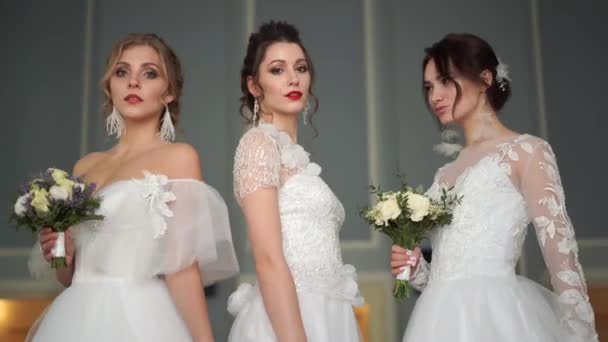 Hochzeitsmode - Porträt von drei schönen Bräuten europäischen Aussehens in Brautkleidern in einem schicken Raum - Filmmaterial, Video