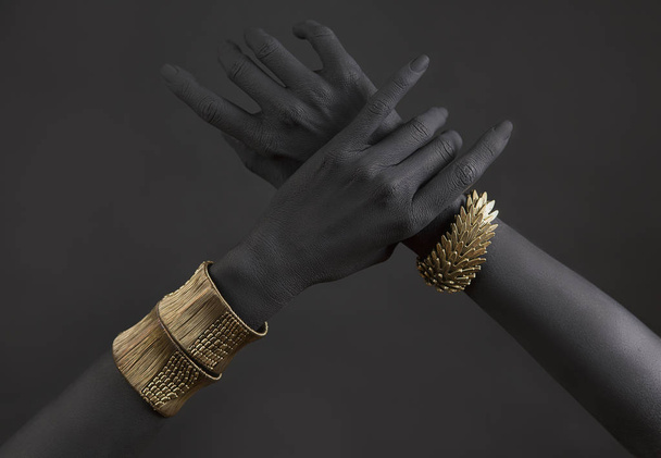 Black woman's hands with gold jewelry. Oriental Bracelets on a black painted hand. Gold Jewelry and luxury accessories on black background closeup. High Fashion art concept  - Foto, imagen