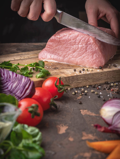 female hands cut raw pork on a wooden board in the kitchen, process of cooking meat with vegetables and spices - Foto, Bild