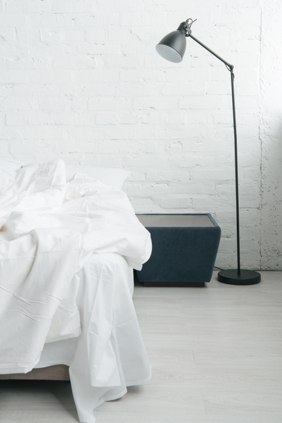 Кровать с белыми простынями и одеялом, лампа и черная тумбочка
  - Фото, изображение