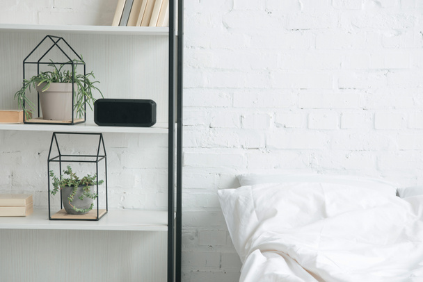 rack with plants, alarm clock and white bed  - Foto, Imagem
