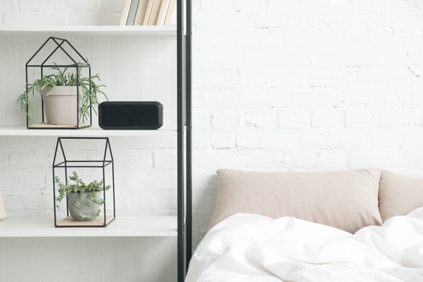 rack with plants, alarm clock and empty bed  - Φωτογραφία, εικόνα