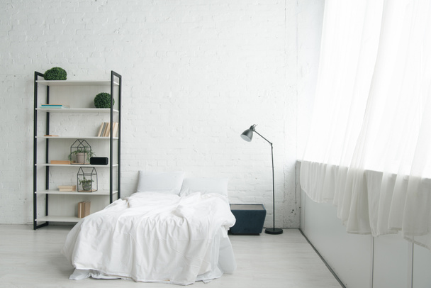 Intérieur de la chambre confortable avec des oreillers sur le lit, table de chevet, lampe et rack
 - Photo, image