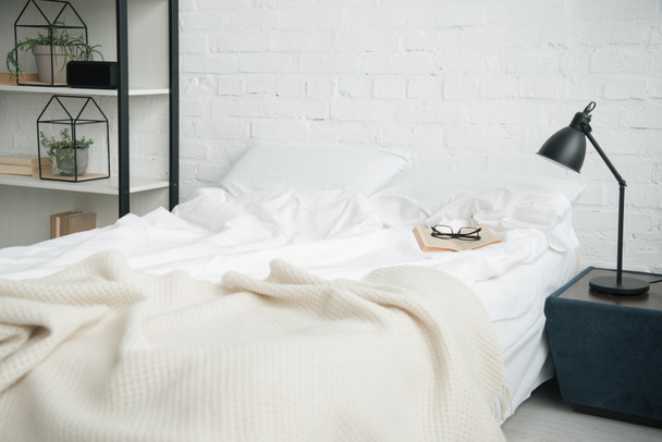 Dormitorio con rack, cama blanca y lámpara en la mesita de noche
 - Foto, imagen