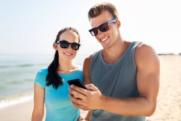 couple in sports clothes with smartphones on beach - Фото, зображення