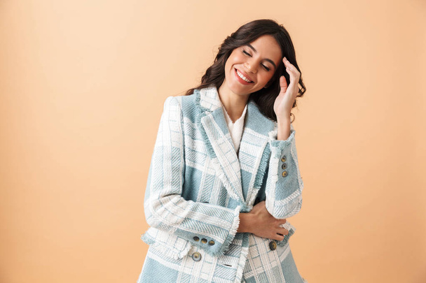 Beautiful brunette woman dressed in plaid jacket posing isolated over beige background - Foto, Imagem