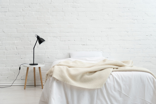 Interior del acogedor dormitorio con almohada en la cama y lámpara en el taburete
 - Foto, imagen