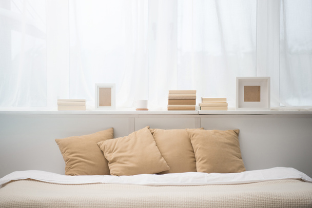 bedroom with brown pillows on bed, books, coffee cup and photo frames  - Photo, Image